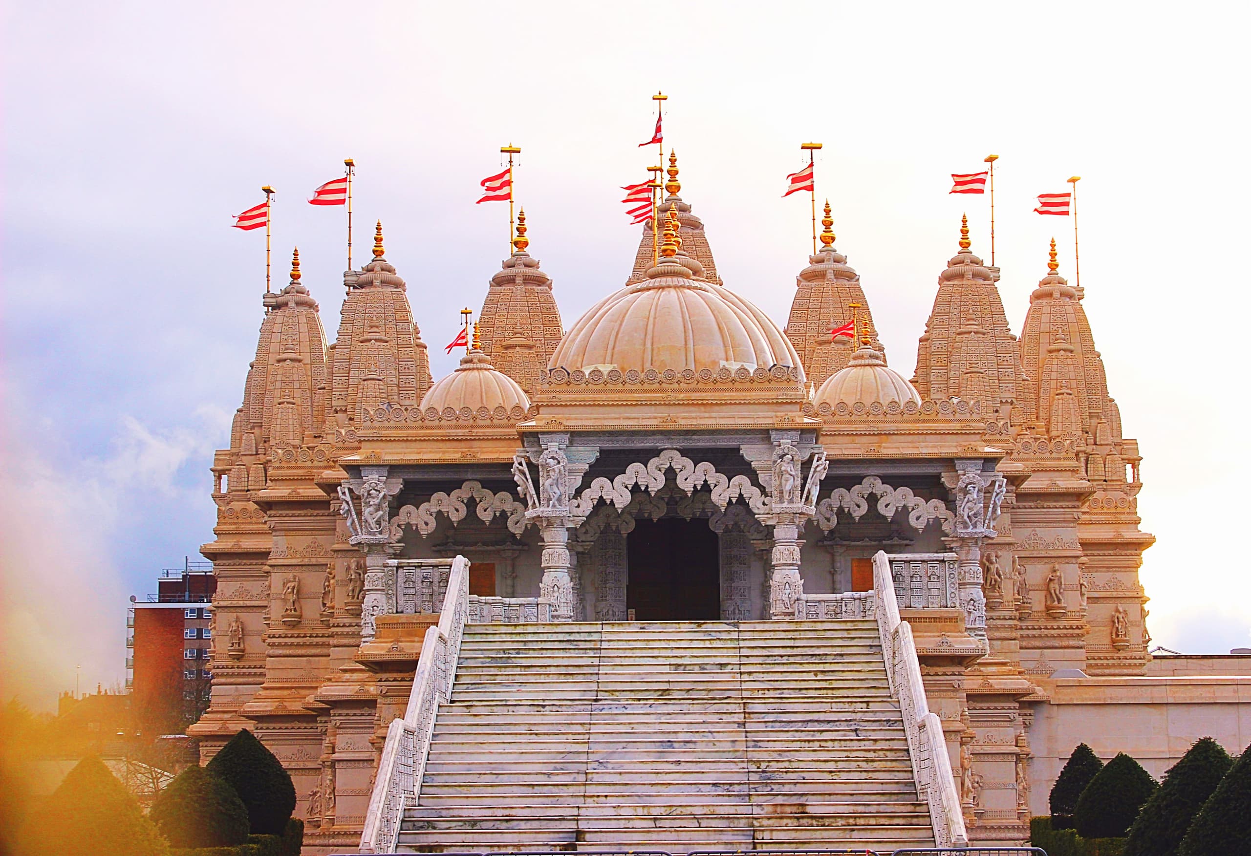 A hand-carved white stone Hindu mandir with many spires and flags, under a pale sky