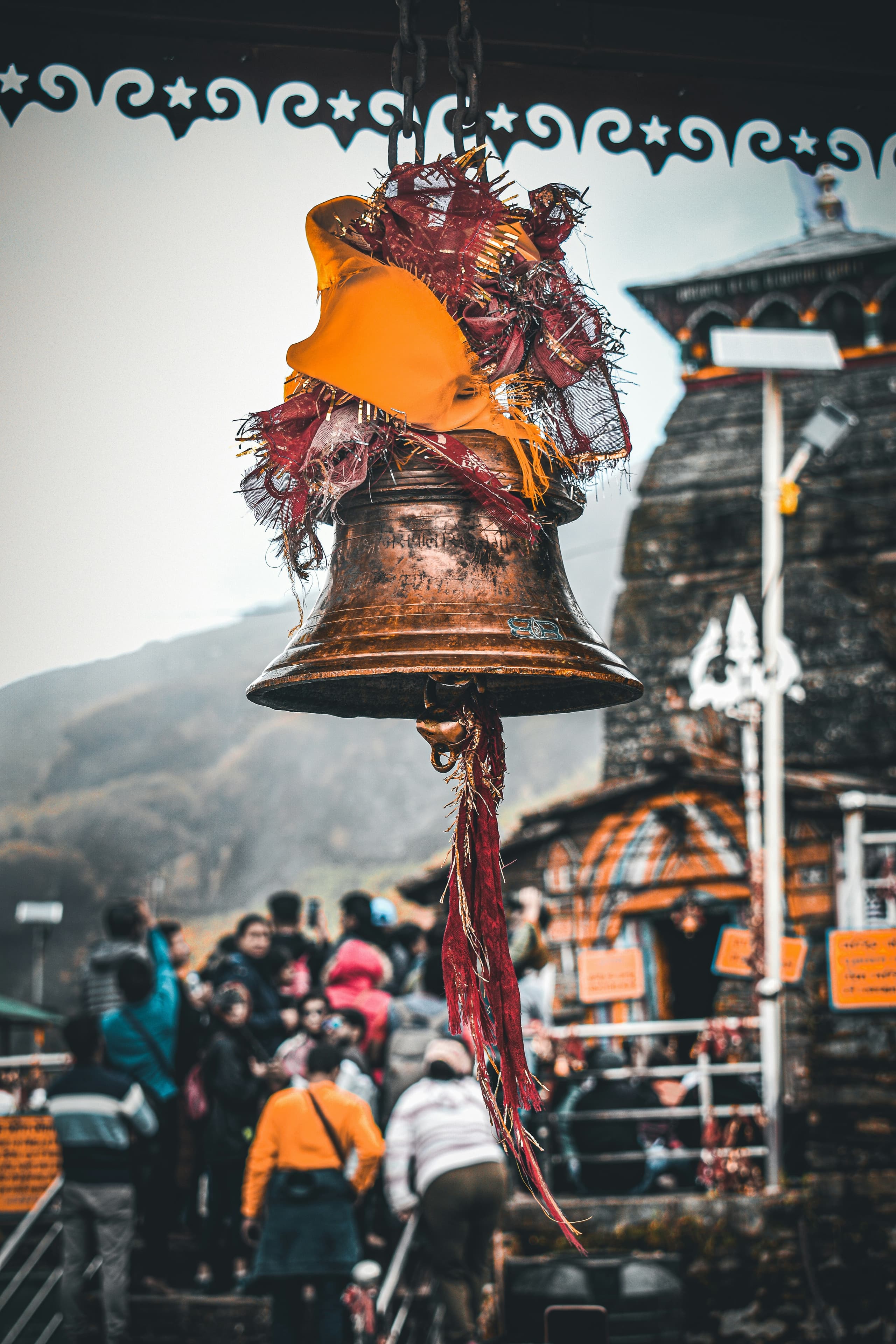 A brass temple bell wrapped in saffron and red cloth, with a stone Himalayan temple behind it